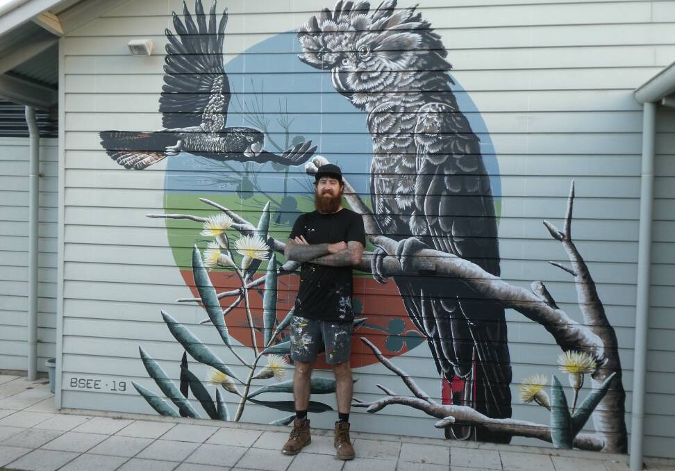 Mural artist Brenton See with a mural he painted in Rockingham that featured male and female red-tailed black cockatoos with a background silhouette of eucalyptus flocktoniae and casuarina.